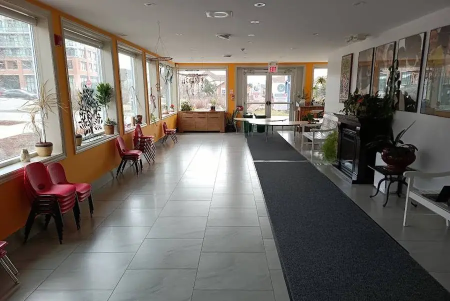 Bright community hall with large windows, plants and a long runner rug