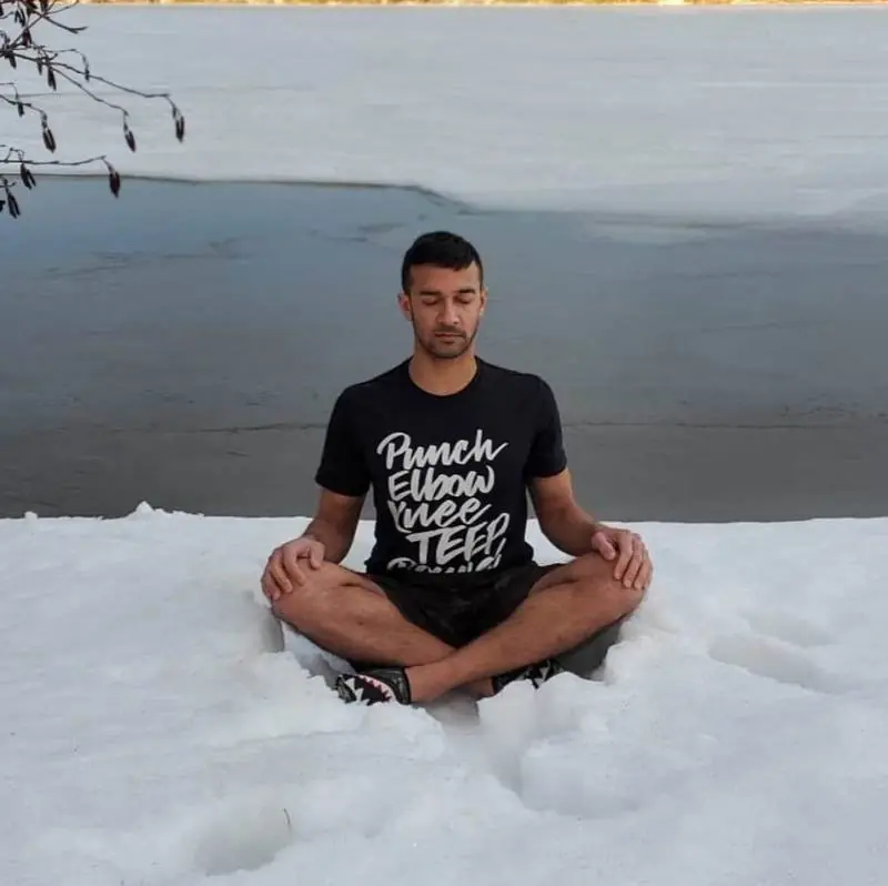 Person meditating cross-legged in snow beside a half-frozen lake